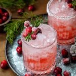 Pink Winter Crown Christmas gin cocktail in a rocks glass with a sugar rim, rosemary sprig, and sugared cranberries.