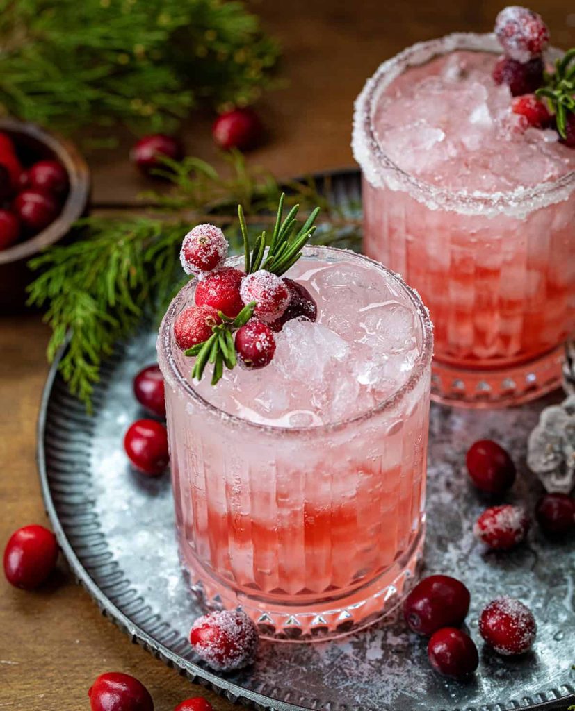 Pink Winter Crown Christmas gin cocktail in a rocks glass with a sugar rim, rosemary sprig, and sugared cranberries.