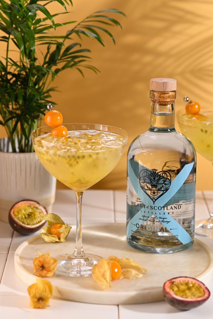 Passion Fruit Fizz cocktail with Heart of Scotland Original Gin, fresh passion fruit, ice and golden berry garnish beside the bottle.